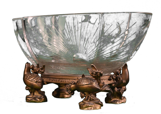 Baccarat, coupe au paysage japonisant, vers 1880   Son décor gravé à la roue se détache sur un cristal d’une grande pureté. Il s’agit d’un paysage japonisant : des oies sauvages s’envolent au-dessus d’une mer, dont les vagues moulées rappellent celles de Kanagawa par Hokusai.    À l’arrière émerge un immense soleil rappelant le surnom du Japon, le « pays du soleil levant ».   La coupe repose sur une monture en bronze doré agrémentée de quatre perdrix, perchées sur des branches chargées de fruits ou de fleurs. Deux d’entre elles picorent des fruits.   Fondée sous Louis XV, la manufacture de cristal française Baccarat fit montre de son excellence aux Expositions Universelles tout au long du XIXe siècle.  Le cachet de Baccarat, apposé à partir de 1875, se trouve sous la base de la monture.    Baccarat créa une autre coupe au décor tout aussi japonisant, soufflée dans une forme identique, dont les détails sont soulignés d’or et de brun. Elle repose également sur une monture en bronze doré japonisante. 